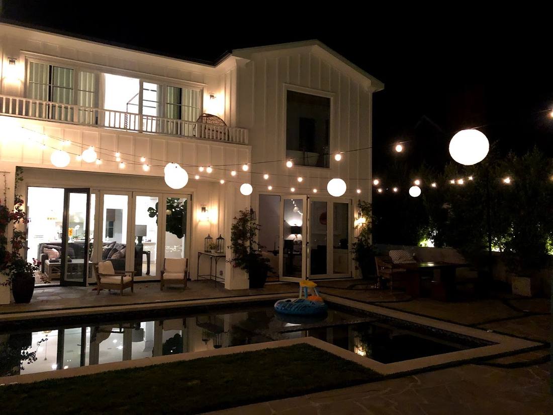 Globe string lights strung over a backyard pool at dusk